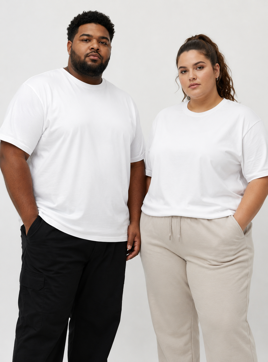 Two models wearing plain white crewneck t-shirts, standing against a light gray studio background. The model on the left wears black cargo pants, and the model on the right wears beige drawstring sweatpants.