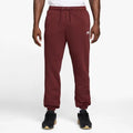 A person wearing maroon Nike sweatpants with a drawstring waist, paired with black sneakers, shown from the waist down on a light gray studio background.