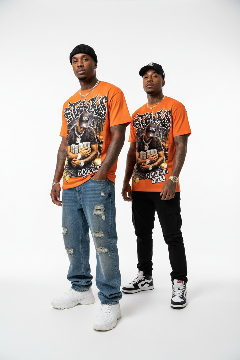 Two men modeling matching orange graphic t-shirts with a large black and white print, styled with distressed blue jeans, black pants, and white sneakers against a plain white studio background.